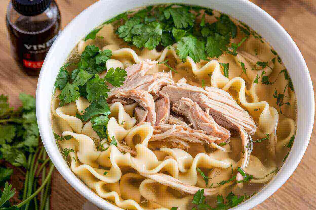 Steaming chicken noodle soup with a bottle of vinegar.